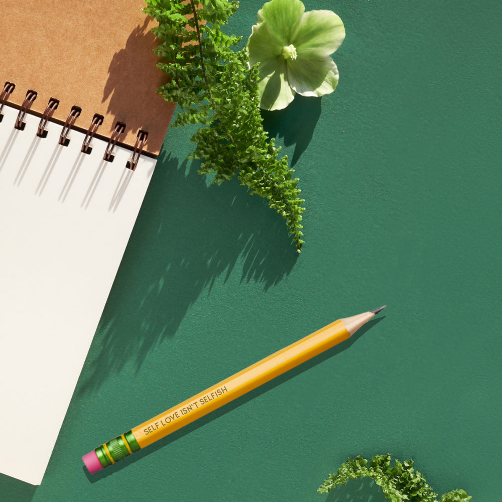 image showing a open notepad with pencil next to it on green background with some green decorative plants around it