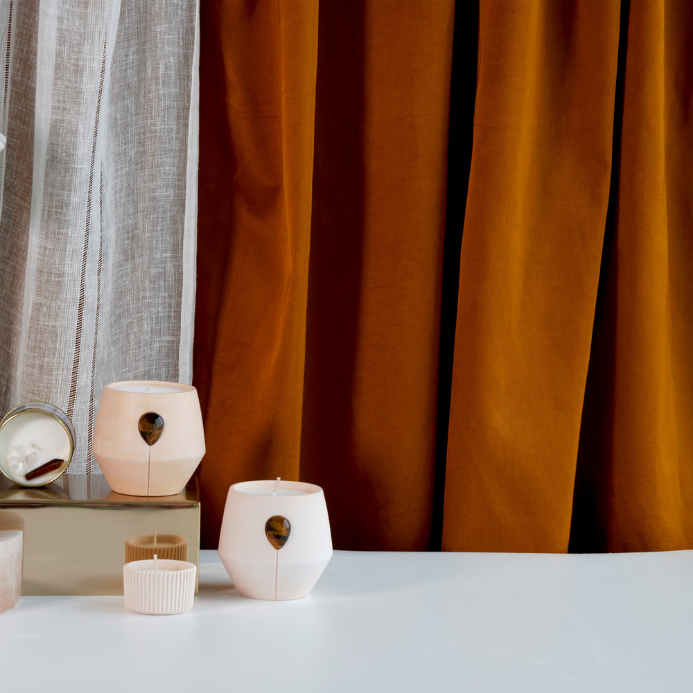 Amber Oro candles Luna, Keepsake and Tealight cup in a stylized image with orchid and royal sunburnt orange and linen fabric draped behind. 
