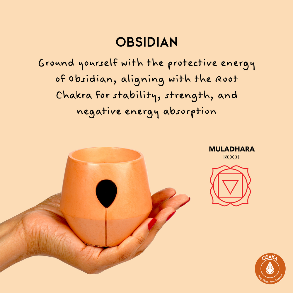 Image of Luna Osaka candle in a hand with the aligned chakra symbol and text that reads: Ground yourself with the protective energy of obsidian, aligning with the root chakra for stability, strength and negative energy absorption. 