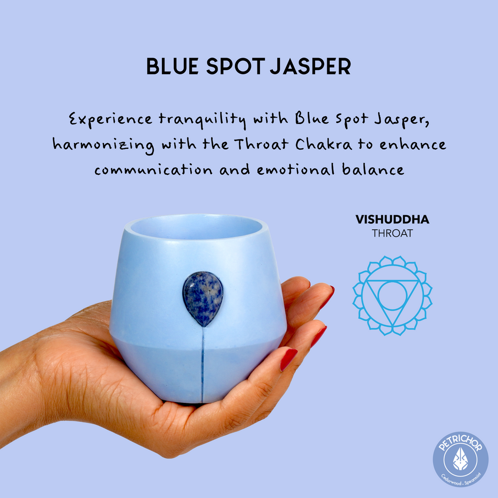 Image of Luna Petrichor candle in a hand with the aligned chakra symbol and text that reads: Expereince tranquility with blue spot jasper harmonising with the throat chakra to enhance communication and emotional balance. 