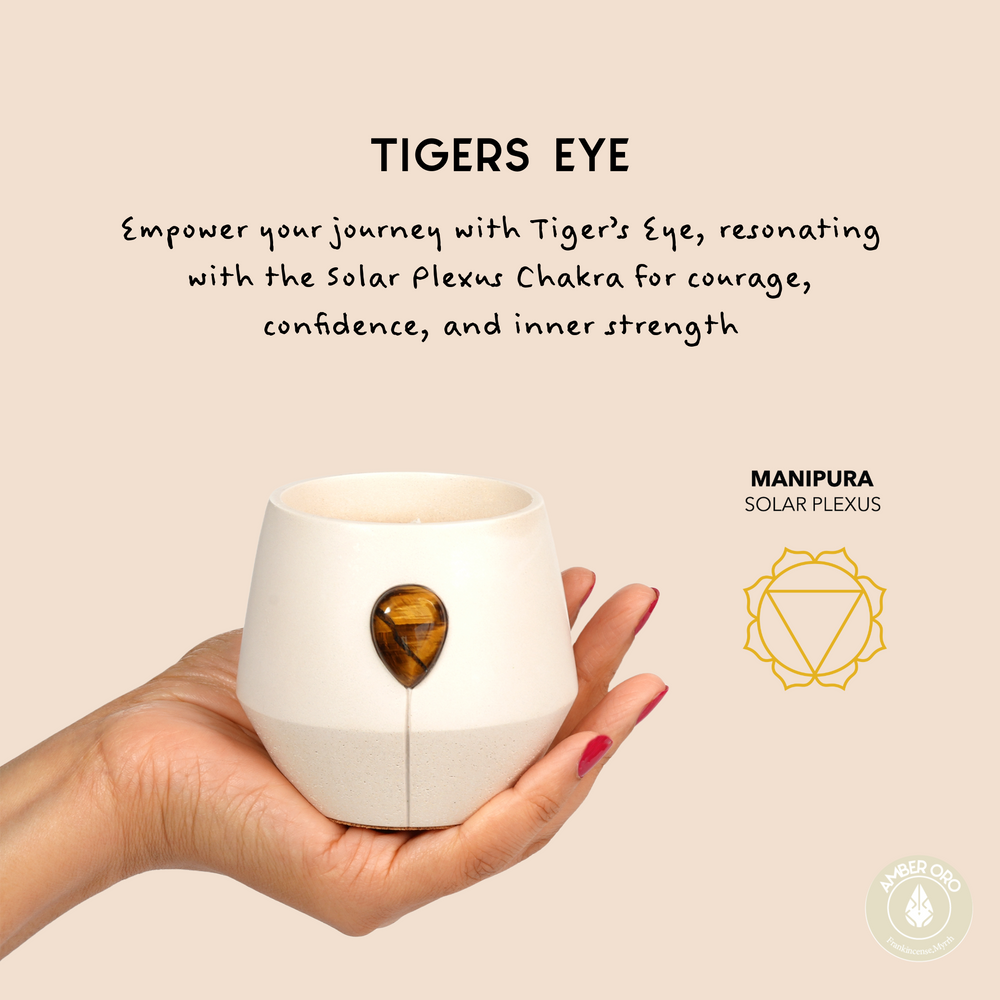 Image of Luna Amber Oro candle in a hand with the aligned chakra symbol and text that reads: Empower your journey with Tigers eye, resonating with the solar plexus chakra for courage, confidence and inner strength. 